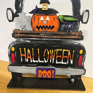May include: Black wooden Halloween truck with a jack-o-lantern, witch hat, and cauldron. The truck has a sign that says "HALLOWEEN" and a license plate that says "BOO!"