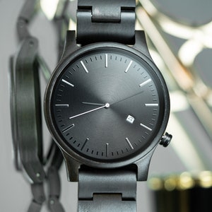 May include: A black wristwatch with a black band and a black face. The watch has white hands and hour markers.