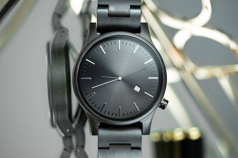 May include: A black wristwatch with a black band and a black face. The watch has white hands and hour markers.