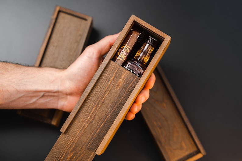 May include: A wooden box with a lid open, revealing a small bottle of liquor and a cigar. The box is made of dark wood with a natural grain.