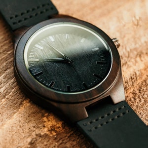 May include: A dark brown wooden wristwatch with a black face and black leather band.