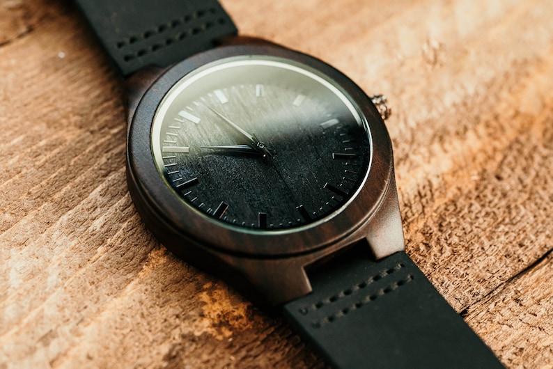 May include: A dark brown wooden wristwatch with a black face and black leather band.