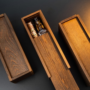 May include: Three wooden boxes, two closed and one open. The open box contains a small bottle and a cigar.