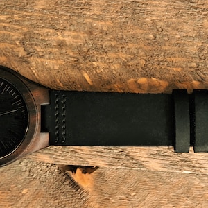 May include: A dark brown wooden wristwatch with a black leather band and a silver buckle.
