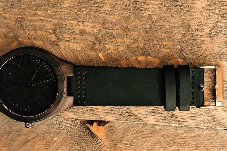 May include: A dark brown wooden wristwatch with a black leather band and a silver buckle.