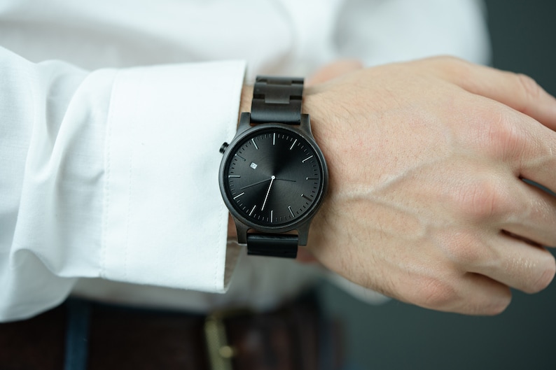 May include: A black wristwatch with a wooden band. The watch face is black with white hands and a small white square at the 12 o'clock position.