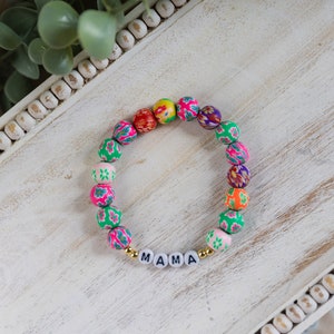 Könnte beinhalten: Ein farbenfrohes Armband mit Perlen in einem Blumenmuster und dem Wort "MAMA" in goldenen Buchstaben.