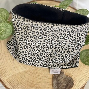 Könnte beinhalten: Ein Halswärmer mit Leopardenmuster in Beige und Schwarz, mit schwarzem Innenfutter. Der Schlauchschal wird auf einer Holzoberfläche präsentiert. Ein kleines Etikett trägt die Aufschrift "Handmade by Selina".