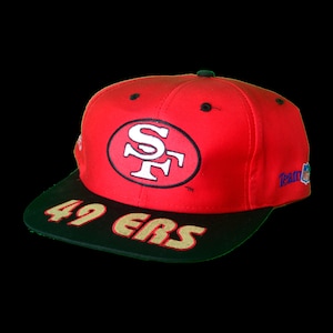 Puede incluir: Gorra de béisbol roja y negra con el logotipo de los San Francisco 49ers y "49ers" escrito en dorado en la parte delantera.