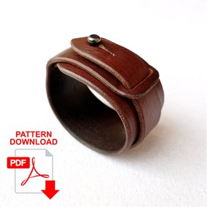 May include: A brown leather bracelet with a simple buckle closure. The bracelet is made of two layers of leather, with the top layer folded over to create a strap. The bracelet is available as a digital download pattern.