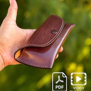 May include: A dark brown leather case with a curved flap and a single snap button closure. The case features visible stitching along the edges and a smooth, polished finish. The image includes a PDF icon and a video tutorial icon at the bottom.