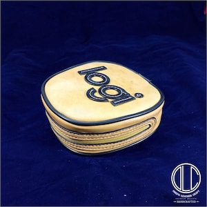 May include: A tan leather round pouch with a zipper closure. The pouch has a black leather logo that says "local" in a circular font.