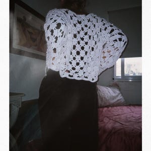 May include: A white crocheted top with a loose, open-weave design. The top has a relaxed fit and a slightly cropped length.