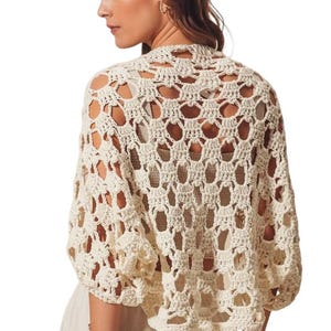 May include: A cream-colored crochet top with a delicate open-stitch pattern. The top has a relaxed fit and three-quarter sleeves.