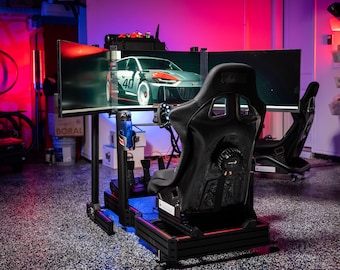 May include: A black racing simulator with a black racing seat, a steering wheel, and pedals. The simulator is set up in a garage with a red and blue light. The simulator is in front of three monitors displaying a racing game.