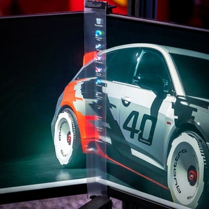 以下が含まれることがあります： 黒色のコンピューターモニターのクローズアップ。モニターには、白と赤のレーシングカーが表示されています。レーシングカーには、「40」と「quattro」の文字が書かれています。背景は濃い緑色です。モニターは黒いスタンドに取り付けられています。