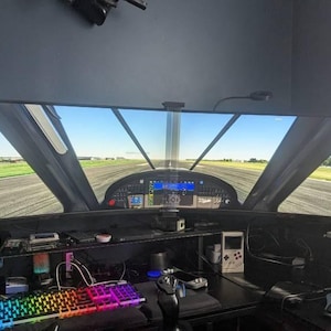 May include: A curved monitor displaying a flight simulator game with a view from the cockpit of a plane on a runway. The monitor is set up on a desk with a keyboard, a joystick, and other gaming accessories.
