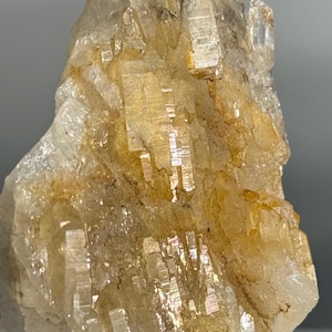 May include: A raw mineral specimen featuring a cluster of translucent, pale yellow and clear crystalline structures with sharp, vertical striations and a jagged, uneven surface texture throughout the entire formation.