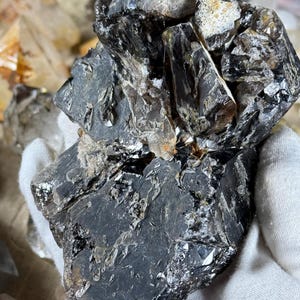 May include: A dark, rough-textured crystal cluster with a mix of black and translucent sections. The crystal has a jagged, irregular shape with reflective surfaces. The overall appearance is of a natural, unpolished mineral specimen.