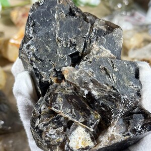 May include: A large, rough-hewn, dark gray crystal with areas of lighter gray and white. The crystal has a complex, layered structure with visible fractures and inclusions. The overall shape is irregular and natural, showcasing its raw form.