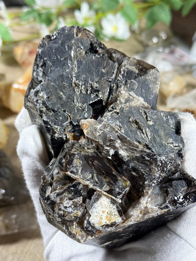 May include: A large, rough-hewn, dark gray crystal with areas of lighter gray and white. The crystal has a complex, layered structure with visible fractures and inclusions. The overall shape is irregular and natural, showcasing its raw form.