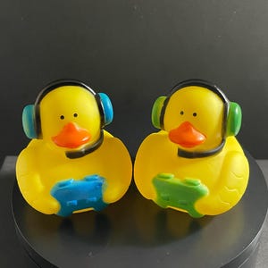 May include: Two yellow rubber duckies wearing black headphones and holding green and blue video game controllers.