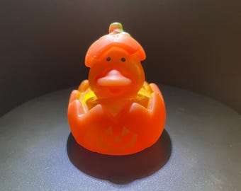May include: Orange rubber duck shaped like a jack-o'-lantern with a green stem and a smiling face.