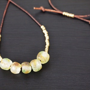 May include: A brown leather cord necklace with gold beads and five large, round, green and yellow glass beads.
