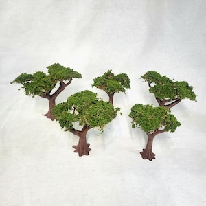 Op de afbeelding: Vijf miniatuurbomen met bruine stammen en levendig groen gebladerte. De bomen hebben een textuur, met de bladeren die dicht en vol lijken. De bomen zijn gerangschikt op een wit oppervlak, waardoor een naturalistische scène ontstaat.