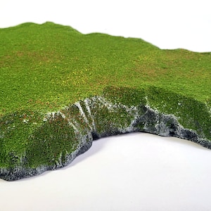 Puede incluir: Una colina verde cubierta de hierba con una base rocosa. La colina es una pieza de terreno en miniatura para juegos de mesa.