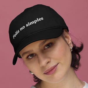 Peut inclure: Casquette de baseball noire avec le texte "Feliz no simples" en blanc. La casquette a une visière incurvée et une coupe structurée. Le chapeau est fait d'un tissu durable et convient à un usage quotidien.