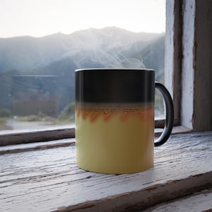 May include: A black and yellow color-changing mug with the inscription "One Ring to rule them all, One Ring to find them, One Ring to bring them all and in the darkness bind them" in Elvish script. Steam rises from the mug, which is sitting on a wooden surface.