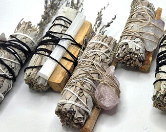 May include: An assortment of sage bundles, palo santo sticks, and crystals. The bundles are wrapped with twine and black or white string. Some bundles include lavender sprigs and crystals in shades of clear, brown, and pink.