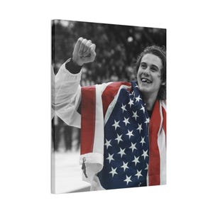 May include: A canvas print featuring a young person wrapped in an American flag, celebrating with a raised fist. The image is in color, with the background in black and white.