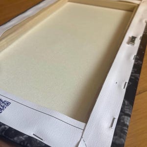 Peut inclure: L'arri&egrave;re d'une toile tendue avec une bordure blanche et des agrafes qui maintiennent la toile au cadre. Le cadre est noir et blanc avec un motif floral.