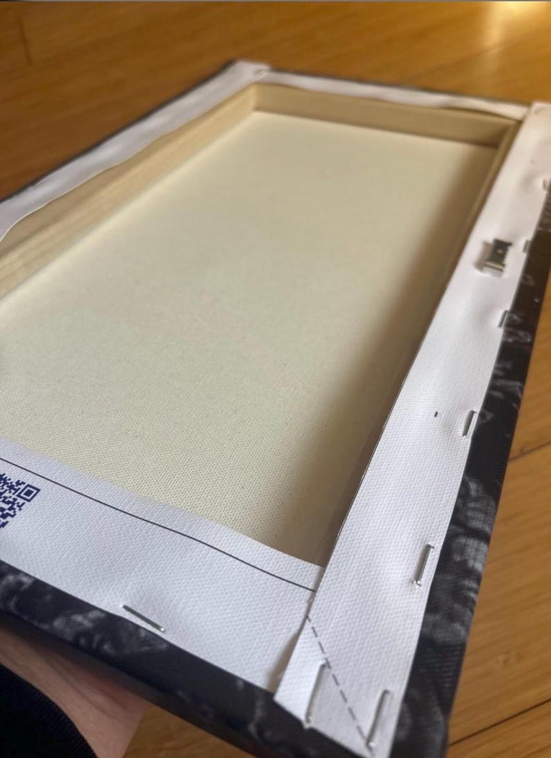 Peut inclure: L'arri&egrave;re d'une toile tendue avec une bordure blanche et des agrafes qui maintiennent la toile au cadre. Le cadre est noir et blanc avec un motif floral.