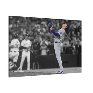 May include: A canvas print of a baseball player in a gray and blue uniform, celebrating with a glove raised. The background is in black and white, with a crowd of people. The player is wearing a blue cap and gray pants.