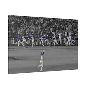 以下が含まれることがあります： 野球の試合の白黒写真。青いアクセントの白いユニフォームを着た選手が腕を上げて祝っています。青と白のユニフォームを着た他の選手が彼に向かって走っています。背景には歓声が上がるファンの群衆がいます。