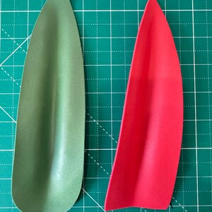 May include: Two teardrop-shaped foam pieces, one olive green and one bright red, are displayed against a green grid background. The shapes are smooth and curved, with a slight indentation along one side, suggesting they may be part of a larger design or craft project.