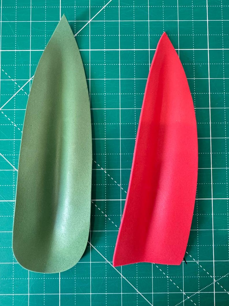 May include: Two teardrop-shaped foam pieces, one olive green and one bright red, are displayed against a green grid background. The shapes are smooth and curved, with a slight indentation along one side, suggesting they may be part of a larger design or craft project.