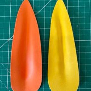 May include: Two teardrop-shaped objects, one orange and one yellow, are displayed against a green grid background. The objects have a smooth, matte finish and a slightly curved shape, resembling petals or leaves.