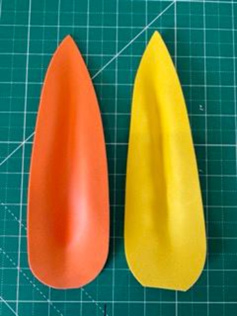 May include: Two teardrop-shaped objects, one orange and one yellow, are displayed against a green grid background. The objects have a smooth, matte finish and a slightly curved shape, resembling petals or leaves.