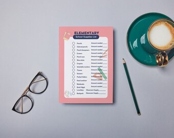 May include: A pink Elementary School Supplies List notepad with a checklist of items like pencils and crayons. A green pencil, a teal coffee cup with gold trim, and a pair of glasses are also on the gray surface.