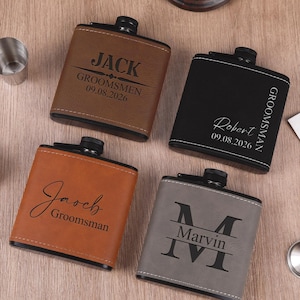 May include: Four square-shaped metal flasks wrapped in faux leather in brown, black, tan, and gray. Each flask features a black screw-top cap and custom laser-engraved text including names like Jack, Robert, Jacob, and Marvin, along with dates.