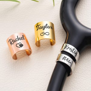 May include: Three personalised stethoscope charms in gold, rose gold, and silver. The gold charm says "Taylor" with an infinity symbol. The rose gold charm says "Rachel" with a heart. The silver charm says "Kristin" and has a leaf design.