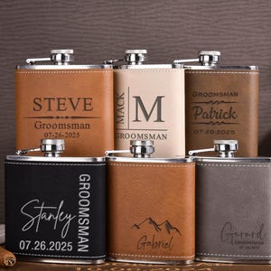May include: Six personalised leather-wrapped hip flasks with engraved names and dates. The flasks are brown, black, grey, and beige.
