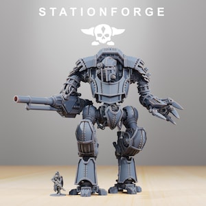 Könnte beinhalten: Ein detailliertes graues Modell einer großen Kriegsmaschine mit Kanonenarm und Klauenhand, neben einer kleinen Soldatenfigur. Der Text "STATIONFORGE" und ein Totenkopf-Logo befinden sich oben.