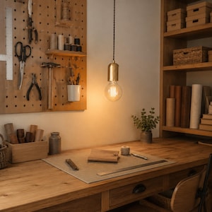 Style A brass plug-in pendant with clear G95 globe bulb lighting an organized craft room workbench and tool pegboard.
