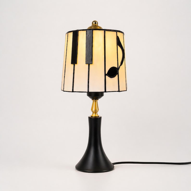 Piano-inspired stained glass table lamp with warm glowing white shade, black piano key accents, and music note design.
