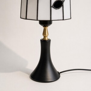 Close-up of the black lamp base with brass-tone accent and lower edge of the stained glass shade.